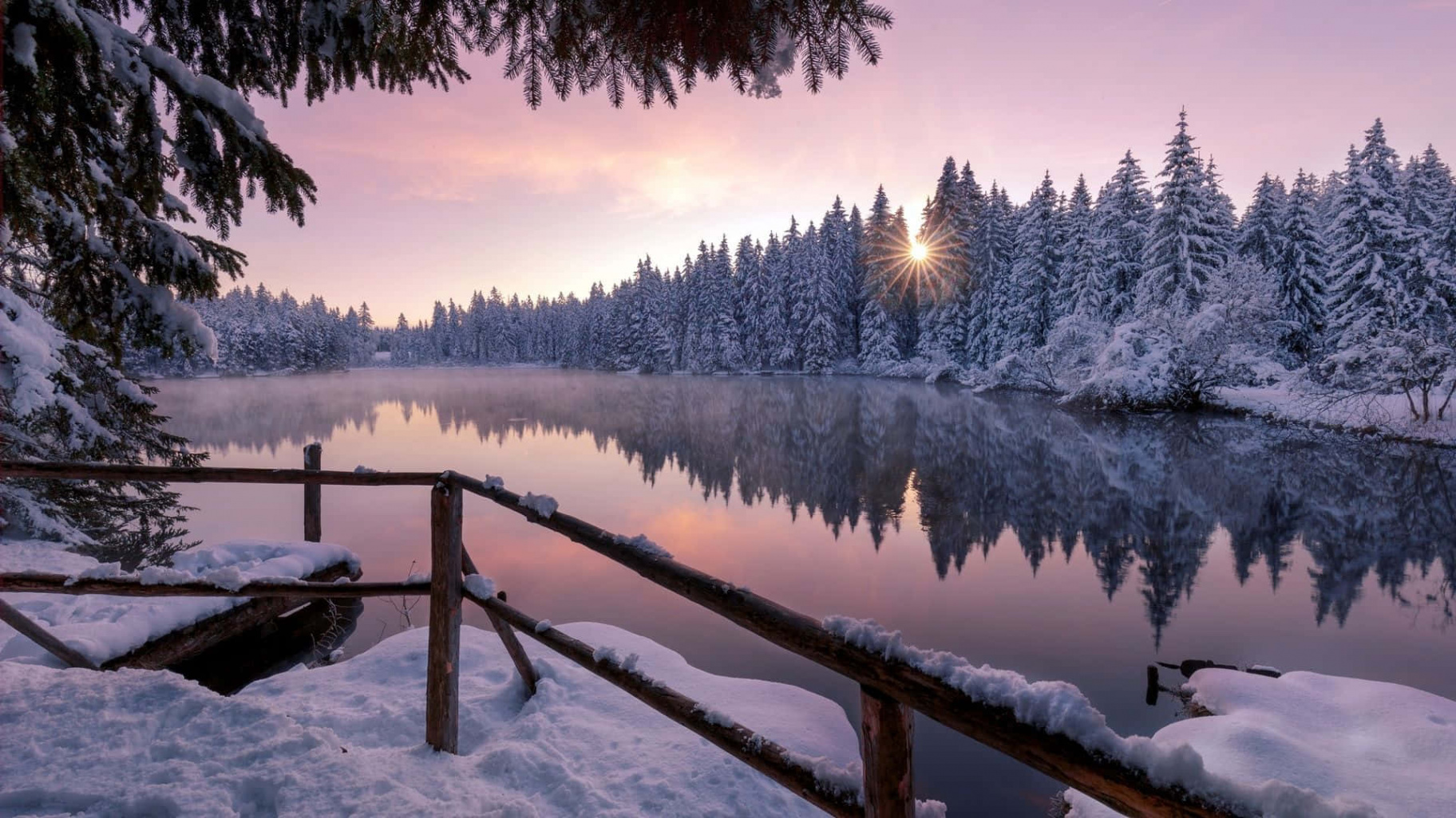 Download A Lake With Snow Covered Trees And A Bridge Wallpaper